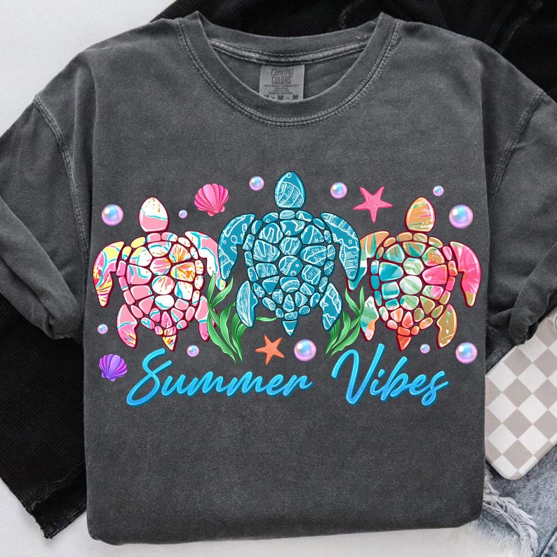 May include: A dark gray t-shirt with a design of three colorful sea turtles with the text "Summer Vibes" in blue.