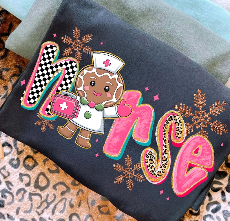 May include: Dark gray sweatshirt with the word "Nurse" in a playful font, featuring a gingerbread nurse character holding a medical bag. The letter "M" has a black and white checkered pattern, and the letter "S" has a leopard print.