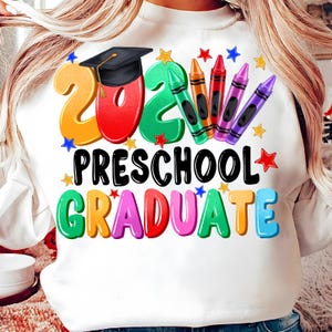 May include: White sweatshirt with a colorful graphic design that says "2024 Preschool Graduate" with a graduation cap and crayons.