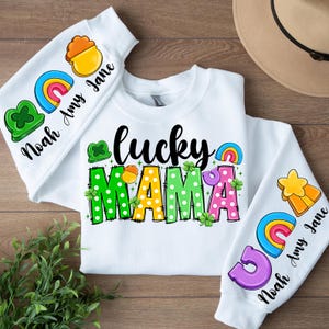 May include: White sweatshirt with the text "lucky mama" in rainbow colors with polka dots. The sleeves have rainbow and shamrock designs with the text "Noah Amy Jane".