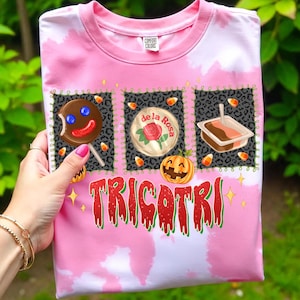 K&ouml;nnte beinhalten: Rosafarbenes T-Shirt mit Batikmuster und einem Halloween-Motiv. Das Design zeigt einen Lebkuchenmann-Lutscher, eine Rose und einen K&uuml;rbis mit dem Wort "TRICOTRI" in Rot und Gr&uuml;n. Hergestellt aus Comfort Colors-Material.