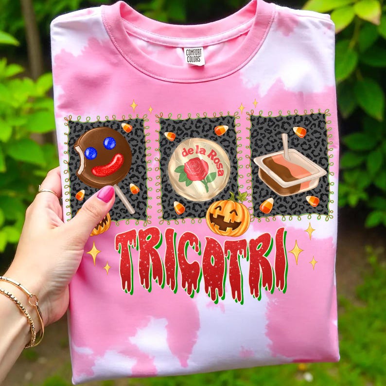 K&ouml;nnte beinhalten: Rosafarbenes T-Shirt mit Batikmuster und einem Halloween-Motiv. Das Design zeigt einen Lebkuchenmann-Lutscher, eine Rose und einen K&uuml;rbis mit dem Wort "TRICOTRI" in Rot und Gr&uuml;n. Hergestellt aus Comfort Colors-Material.