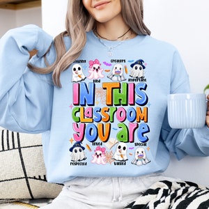 May include: Light blue sweatshirt with a colorful graphic of ghosts and the text "In this classroom you are amazing, kind, creators, loved, respected, valued, important, special".
