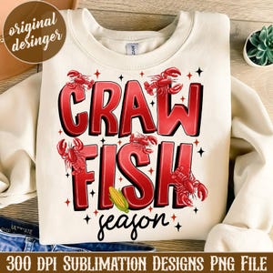 May include: A white sweatshirt with the text "Crawfish Season" in red letters. The text is surrounded by images of crawfish.
