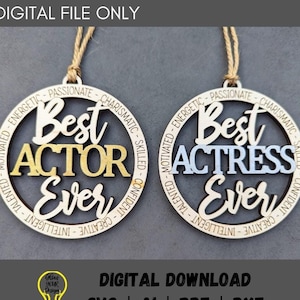 Puede incluir: Dos adornos de madera con un diseño circular. El adorno superior dice "Best Actor Ever" en letras doradas. El adorno inferior dice "Best Actress Ever" in letras azules. Ambos adornos tienen una cuerda para colgar.