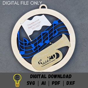 May include: A wooden ornament with a gold tuba and blue musical notes. The ornament has a white flag with the text "Charlotte Smith Eagle Point High 2022-2023".