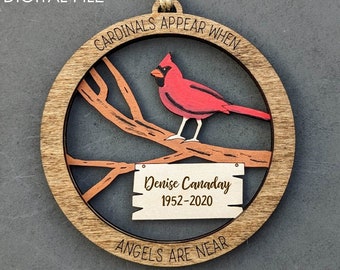 May include: A wooden ornament featuring a red cardinal perched on a branch with a sign that reads "Denise Canaday 1952-2020". The ornament is surrounded by the text "Cardinals Appear When Angels Are Near".