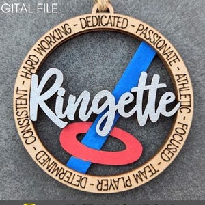 May include: A wooden ringette ornament with the word "Ringette" in white lettering. The ornament is decorated with a blue and red ringette stick and a blue and red ring. The ornament is surrounded by a circle of text that reads "Working - Dedicated - Passionate - Athletic - Focused - Team Player - Determined - Consistent".