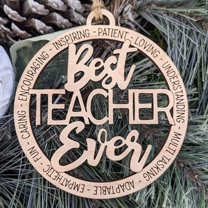 Peut inclure: Ornement en bois avec le texte "Best Teacher Ever" entour&eacute; d'un cercle d'adjectifs positifs d&eacute;crivant un enseignant, tels que "inspirant", "patient", "aimant", "compr&eacute;hensif", "attentionn&eacute;", "amusant", "empathie", "adaptable" et "multit&acirc;che".