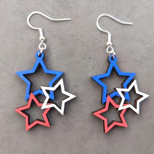 May include: A pair of dangle earrings featuring three layered stars. The stars are red, white, and blue.