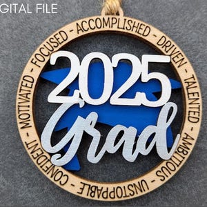 May include: A wooden ornament with a blue and white graduation cap design. The ornament features the year "2025" and the word "Grad" in a silver script font. The ornament is surrounded by a circle of text that reads "Motivated - Focused - Accomplished - Driven - Talented - Ambitious - Unstoppable - Confident".