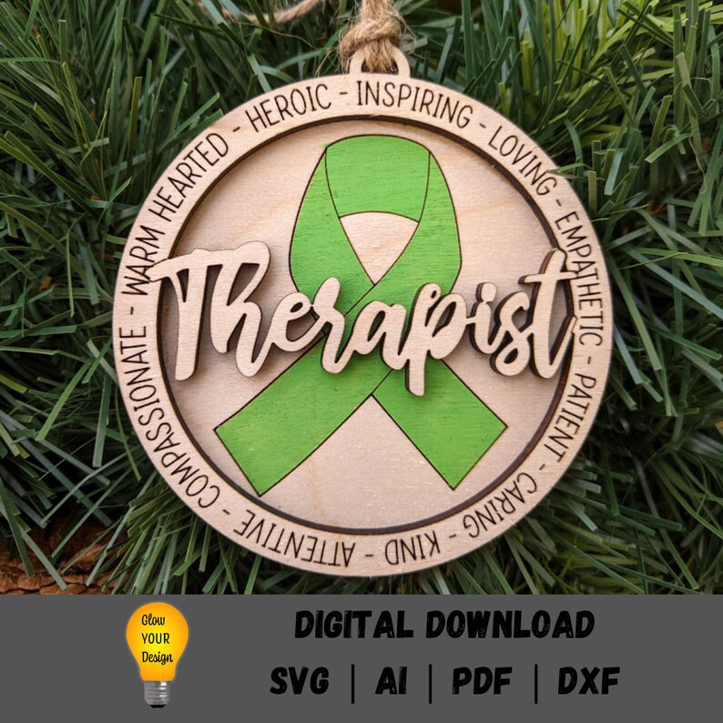 May include: A wooden ornament with a green ribbon and the word "Therapist" in a decorative font. The ornament is surrounded by a circle of text that reads "Warm Hearted - Heroic - Inspiring - Loving - Empathetic - Patient - Caring - Kind - Attentive - Compassionate".