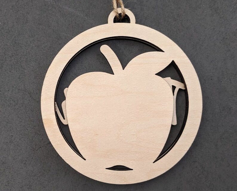 May include: A wooden ornament shaped like an apple with a cutout design. The ornament is a light brown color and has a string attached to the top for hanging.
