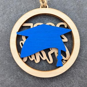 May include: A wooden round ornament with a blue graduation cap cutout and the text "Class of 2023" in white.
