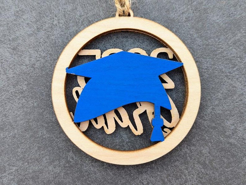 May include: A wooden round ornament with a blue graduation cap cutout and the text "Class of 2023" in white.
