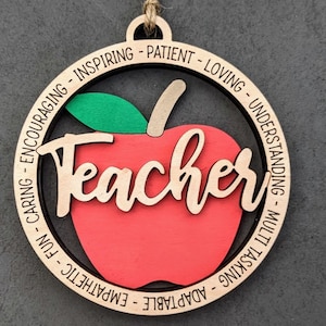 May include: Wooden apple ornament with the word "Teacher" in the center and a list of positive adjectives around the edge, including "adaptable", "empathetic", "fun", "caring", "encouraging", "inspiring", "patient", "loving", "understanding", "multi-tasking".