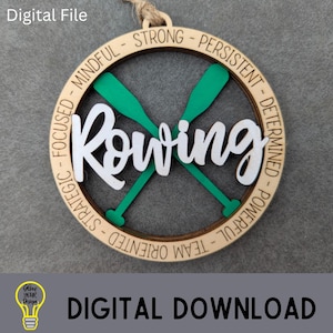 Peut inclure: Ornement en bois sur le thème de l'aviron avec le mot "Rowing" en écriture blanche, des rames vertes et des mots de motivation sur le bord. L'ornement est un téléchargement de fichier numérique.