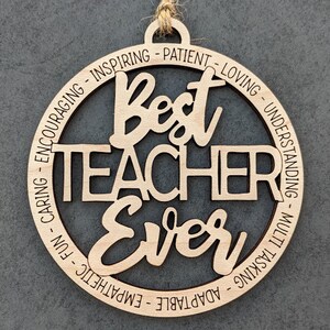 Peut inclure: Ornement en bois avec le texte "Best Teacher Ever" entour&eacute; d'un cercle d'adjectifs positifs d&eacute;crivant un enseignant, tels que "inspirant", "patient", "aimant", "compr&eacute;hensif", "adaptable", "empathie", "amusant", "attentionn&eacute;" et "encourageant".