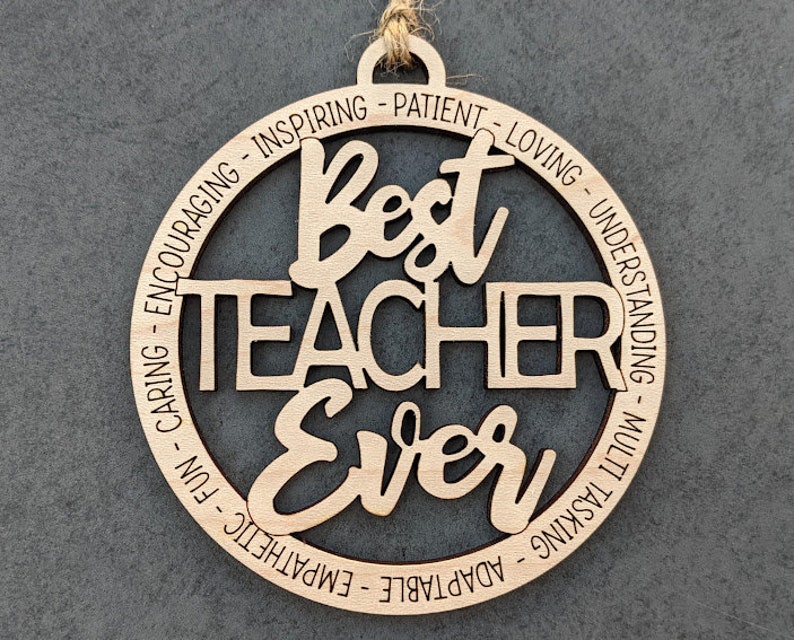 Peut inclure: Ornement en bois avec le texte "Best Teacher Ever" entour&eacute; d'un cercle d'adjectifs positifs d&eacute;crivant un enseignant, tels que "inspirant", "patient", "aimant", "compr&eacute;hensif", "adaptable", "empathie", "amusant", "attentionn&eacute;" et "encourageant".