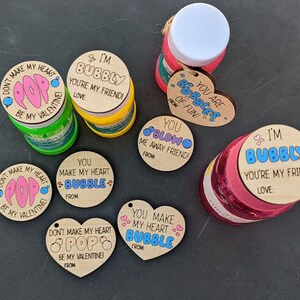 Puede incluir: Surtido de botellas de soluci&oacute;n de burbujas con tem&aacute;tica del D&iacute;a de San Valent&iacute;n con etiquetas de madera. Las etiquetas tienen varios mensajes, que incluyen "No hagas que mi coraz&oacute;n explote, &iexcl;s&eacute; mi Valent&iacute;n!" y "&iexcl;Eres burbujas de diversi&oacute;n!"