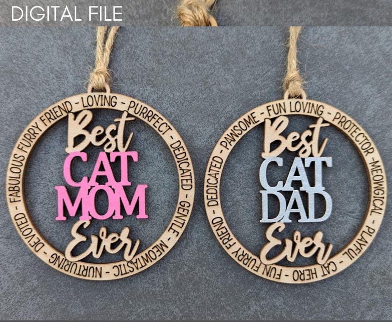 May include: Two wooden ornaments with a circular design. The ornament on the left says "Best Cat Mom Ever" in pink and white lettering. The ornament on the right says "Best Cat Dad Ever" in white and gray lettering.
