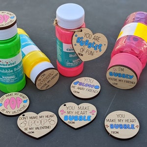 Puede incluir: Una colecci&oacute;n de seis botellas de soluci&oacute;n de burbujas con tem&aacute;tica del D&iacute;a de San Valent&iacute;n con etiquetas de madera. Las etiquetas tienen varios mensajes, que incluyen "You are Bubbles of Fun!" y "You Make My Heart Bubble".