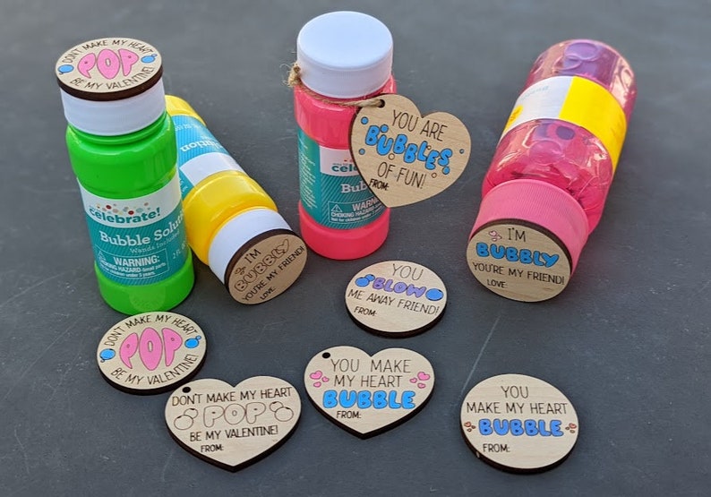 Puede incluir: Una colecci&oacute;n de seis botellas de soluci&oacute;n de burbujas con tem&aacute;tica del D&iacute;a de San Valent&iacute;n con etiquetas de madera. Las etiquetas tienen varios mensajes, que incluyen "You are Bubbles of Fun!" y "You Make My Heart Bubble".