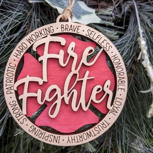 Puede incluir: Adorno de Navidad de madera con forma de hidrante con las palabras "Fire Fighter" en el centro. El adorno est&aacute; decorado con las palabras "Hard Working, Brave, Selfless, Honorable, Loyal, Trustworthy, Inspiring, Strong, Patriotic" alrededor del borde.