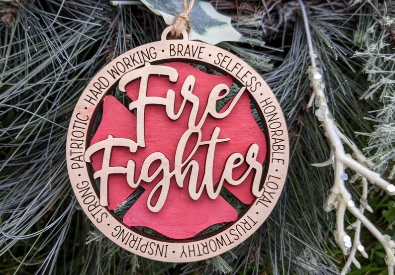 Puede incluir: Adorno de Navidad de madera con forma de hidrante con las palabras "Fire Fighter" en el centro. El adorno est&aacute; decorado con las palabras "Hard Working, Brave, Selfless, Honorable, Loyal, Trustworthy, Inspiring, Strong, Patriotic" alrededor del borde.