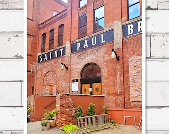 Puede incluir: Un edificio de ladrillo con un letrero que dice "Saint Paul Brewery". El edificio tiene una gran puerta arqueada con puertas dobles. Hay plantas frente al edificio.