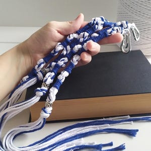 Peut inclure: Un ensemble de cordon macramé bleu et blanc avec des perles argentées et des fermoirs métalliques. Le cordon est noué en un motif de nœuds et a de longues franges.