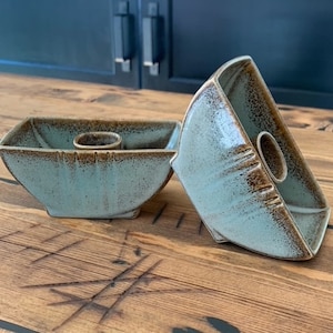 May include: Two teal blue ceramic candle holders with a brown glaze. The candle holders are sitting on a wooden surface.