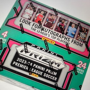 May include: A teal and pink Panini Prizm Premier League Soccer trading card box. The box features images of soccer players and text that reads "Look for autographs from the league's top players!" and "2023-24 Panini Prizm Premier League Soccer."