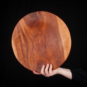 Op de afbeelding: Een grote, ronde houten serveerschaal gemaakt van één stuk hout. De schaal heeft een rijke roodbruine kleur en een natuurlijk houtnerfpatroon.