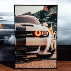 May include: Framed print featuring a white and black sports car with bright orange headlights. The car is partially obscured by smoke, suggesting speed and power. The image is set against a blurred background.