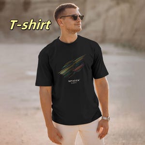 Puede incluir: Camiseta negra con un diseño de líneas diagonales coloridas y el texto "SPACEX FLIGHT 7". La camiseta la lleva una persona con gafas de sol y pantalones blancos.
