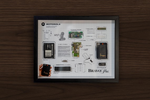 A real Motorola Bravo Plus pager cracked open and mounted as shadow-box wall art — functional circuitry turned into conversation-starting decor.