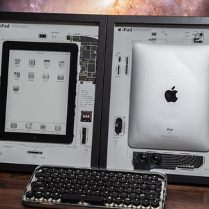 May include: Two framed images of an iPad, one showing the device's internal components and the other showing the back of the device with the Apple logo. The frames are black and the images are on a white background. A black and silver keyboard is in the foreground.