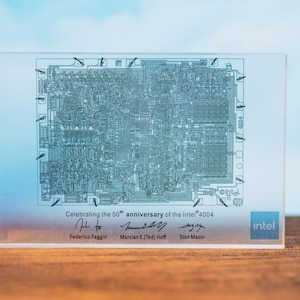 May include: A clear acrylic block featuring a detailed circuit diagram of the Intel 4004 processor. The block commemorates the 50th anniversary of the Intel 4004, with signatures and the Intel logo. The background is a gradient of blue.