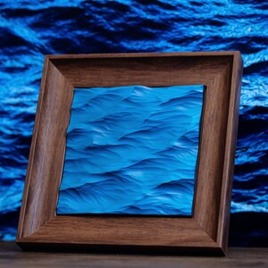 K&ouml;nnte beinhalten: Ein gerahmtes Kunstwerk, das ein blaues Meereswellenmuster darstellt. Der Rahmen ist aus dunklem Holz und hat ein schlichtes Design.