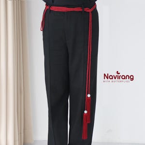 Könnte beinhalten: Schwarze Hose mit rotem geflochtenem Gürtel und Quastendetails. Der Gürtel wird in der Taille getragen und hat eine lange Quaste, die an der Seite der Hose herunterhängt. Der Text "Navirang with Butterflies" ist sichtbar.