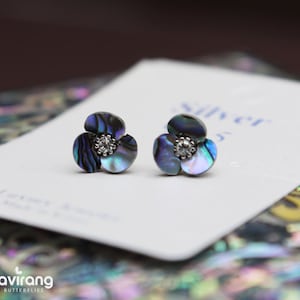 Può includere: Un paio di orecchini d'argento a forma di fiore con accenti di madreperla blu e verde iridescenti e un cristallo trasparente al centro di ogni fiore.