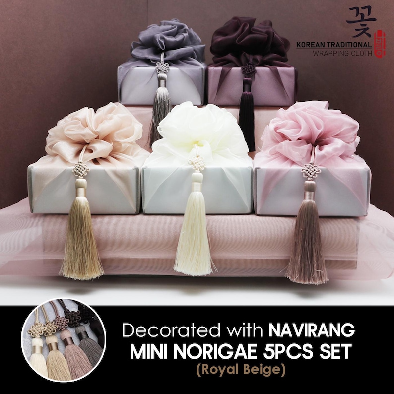May include: Set of five mini Korean traditional gift boxes with decorative fabric tops and tassels. The boxes are in various colors, including beige, pink, and white. The boxes are decorated with the text "Decorated with NAVIRANG MINI NORIGAE 5PCS SET (Royal Beige)".