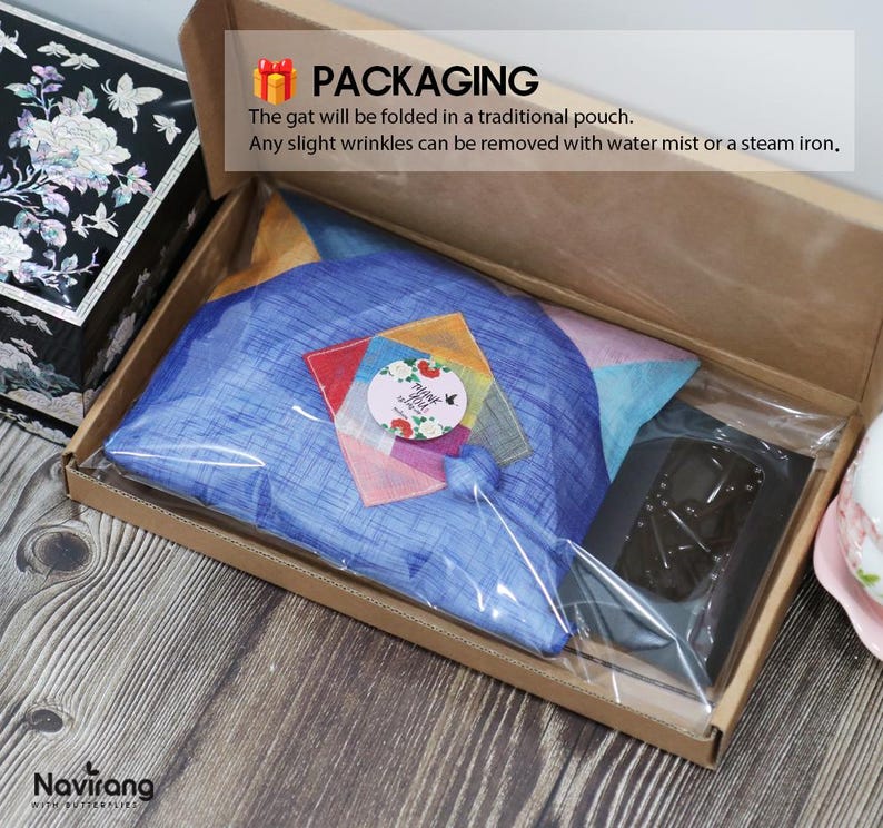 May include: A blue fabric item folded inside a clear plastic bag within a brown cardboard box. The package includes a circular sticker with floral designs and the text Thank You, alongside a black rectangular object and a small colorful patch.