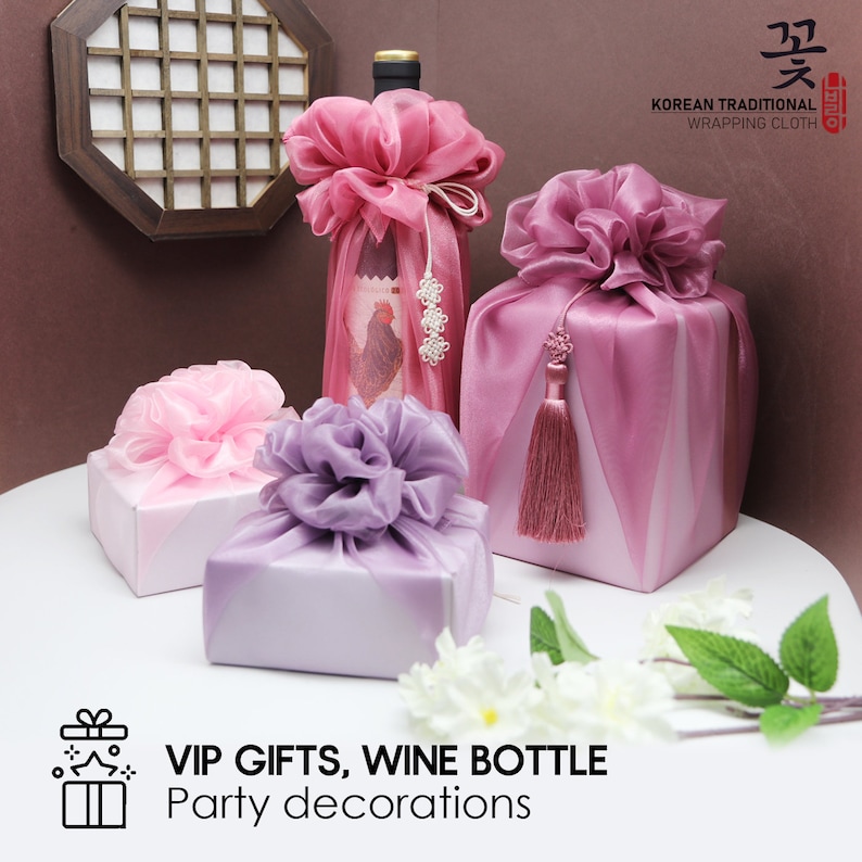 May include: Three gifts wrapped in traditional Korean wrapping cloth, called "Bojagi". The gifts are a wine bottle, a small box, and a larger box. The wine bottle is wrapped in pink and white fabric with a pink flower on top. The small box is wrapped in pink fabric with a pink flower on top. The larger box is wrapped in purple fabric with a purple flower on top. The text "VIP GIFTS, WINE BOTTLE Party decorations" is at the bottom of the image.