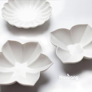 以下が含まれることがあります： 白いセラミック製の皿が3つ。2つは丸みを帯びた花びらの花の形をしており、1つはスカラップのプレートです。皿は白い背景にあります。「Navirang with butterflies」のロゴが右下にあります。