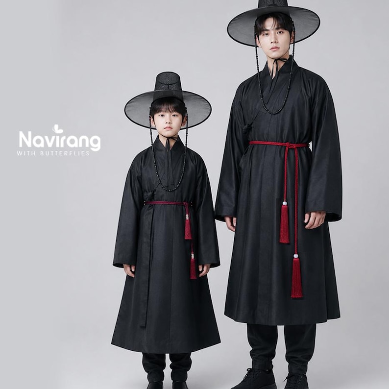 May include: Two individuals wearing black traditional Korean hanbok robes with long sleeves, high collars, and red waist ties featuring hanging tassels. Both wear wide-brimmed black hats with chin straps. The text Navirang WITH BUTTERFLIES is visible.