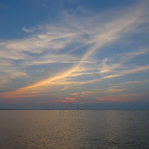May include: A sunset over a calm body of water with a blue and orange sky featuring wispy clouds. The text IGNITE THE SOUL is centered in the lower portion of the image, with a small dragonfly icon positioned directly above the word IGNITE.