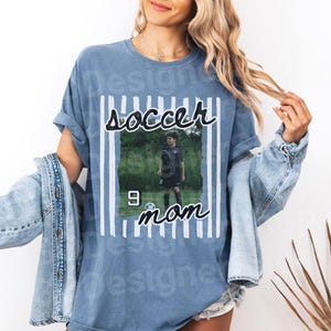 Puede incluir: Camiseta azul con las palabras "soccer mom" y una foto de un jugador de f&uacute;tbol. La camiseta tiene un dise&ntilde;o de rayas verticales y el n&uacute;mero 9. La camiseta es de corte holgado.