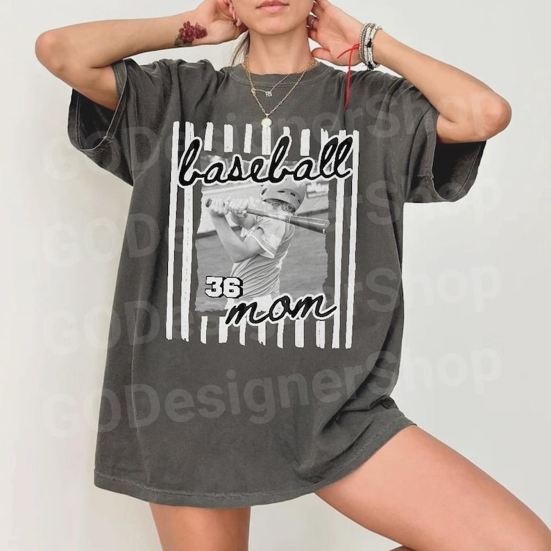 May include: Dark gray t-shirt with a baseball-themed graphic. The design features the word "baseball" in cursive, a black and white image of a baseball player, the number "36", and the word "mom".